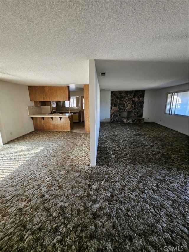 12546 Rain Shadow Rd, Victorville, CA 92395 - unfurnished living room featuring carpet flooring, a textured ceiling, healthy amount of natural light, and a stone fireplace