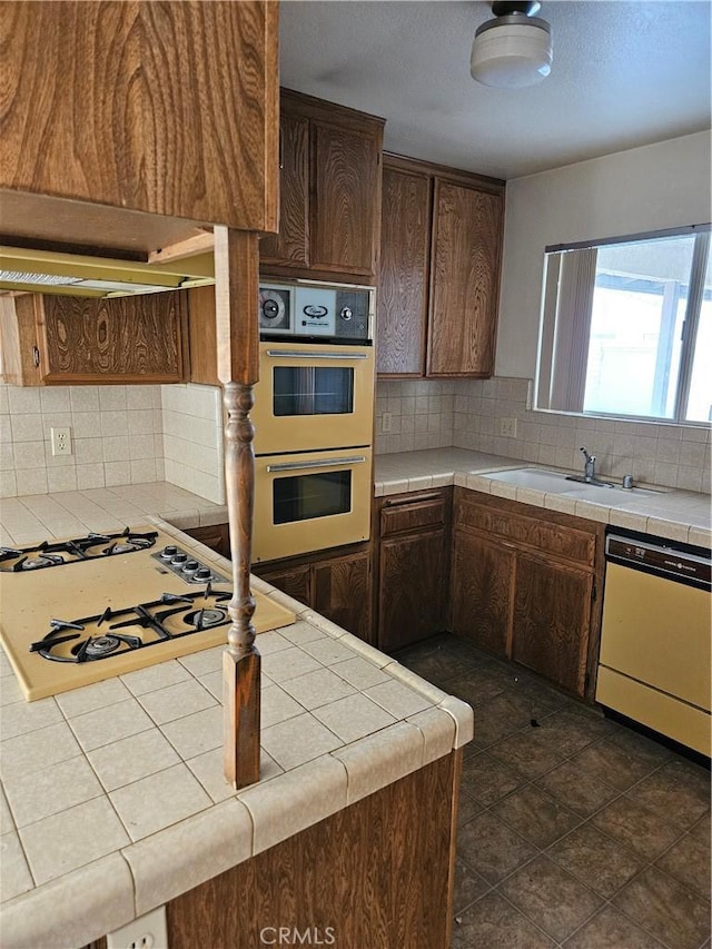 12546 Rain Shadow Rd, Victorville, CA 92395 - kitchen with white dishwasher, tile counters, double wall oven, decorative backsplash, and dark brown cabinetry