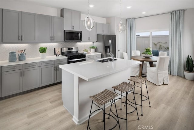 25172 Hunter Ave, Moreno Valley, CA 92551 - kitchen featuring stainless steel appliances, gray cabinetry, tasteful backsplash, a kitchen island with sink, and light wood-style flooring