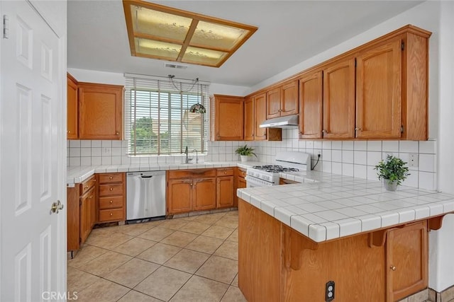 658 Tusky Ave, Los Banos, CA 93635 - kitchen with stainless steel dishwasher, white range with gas stovetop, under cabinet range hood, a peninsula, and brown cabinetry