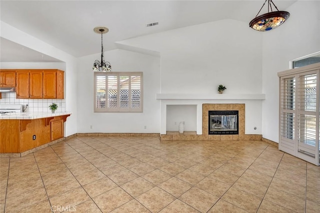 658 Tusky Ave, Los Banos, CA 93635 - unfurnished living room with light tile patterned flooring, healthy amount of natural light, a tiled fireplace, high vaulted ceiling, and a chandelier