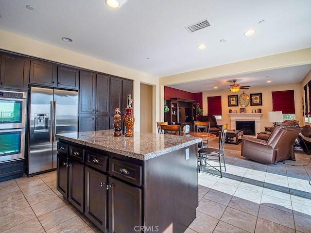 9275 Serenity St, Riverside, CA 92508 - kitchen with appliances with stainless steel finishes, light tile patterned flooring, a center island, a fireplace, and light stone counters