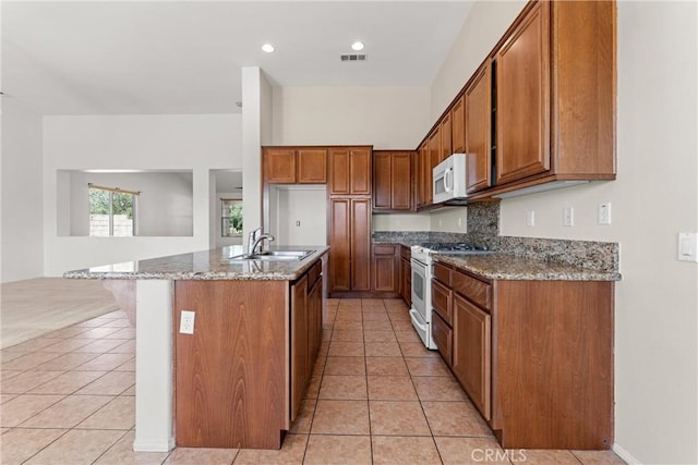 42619 Meridian Way, Lancaster, CA 93536 - kitchen with white appliances, brown cabinets, light tile patterned floors, stone counters, and a kitchen island with sink