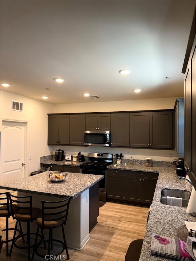12708 Ojo Caliente St, Victorville, CA 92392 - kitchen with stainless steel appliances, light stone counters, a kitchen breakfast bar, a center island, and light wood-type flooring