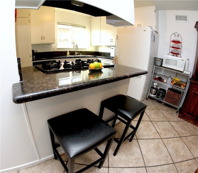 2904 Sterling St, Pomona, CA 91767 - kitchen with white appliances, a peninsula, light tile patterned floors, a breakfast bar, and dark stone counters
