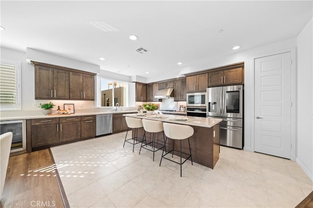 536 Cultivate, Irvine, CA 92618 - kitchen with appliances with stainless steel finishes, beverage cooler, a kitchen breakfast bar, dark brown cabinetry, and recessed lighting