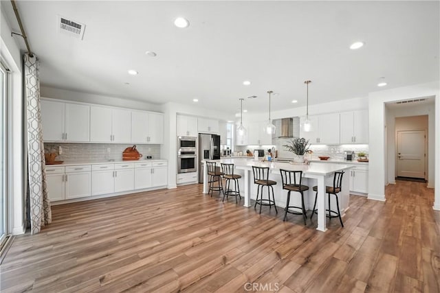 3969 Eliopulos Ranch Dr, Palmdale, CA 93551 - kitchen featuring wall chimney range hood, stainless steel appliances, tasteful backsplash, a kitchen bar, and white cabinetry