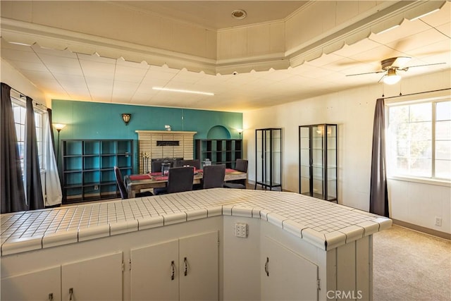 5772 Arrowhead Lake Rd, Hesperia, CA 92345 - kitchen with tile counters, a brick fireplace, a ceiling fan, and light colored carpet