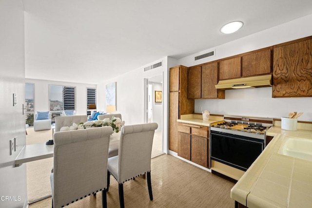 800 W 1st St Unit 1701, Los Angeles, CA 90012 - kitchen featuring white gas stove, brown cabinetry, under cabinet range hood, tile countertops, and open floor plan