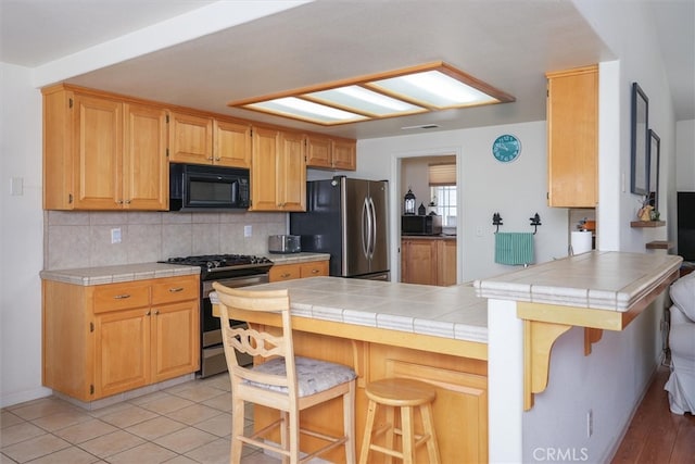 45337 Valley Oak Dr, Ahwahnee, CA 93601 - kitchen featuring appliances with stainless steel finishes, backsplash, a kitchen bar, a peninsula, and tile countertops