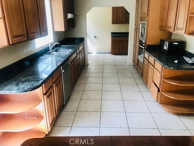 2710 Castle Rock Rd, Diamond Bar, CA 91765 - kitchen with open shelves, stainless steel appliances, light tile patterned floors, dark stone counters, and brown cabinetry