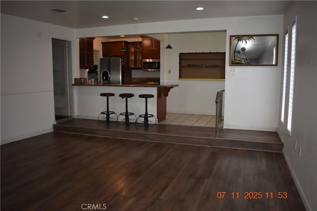 1331 Bothwell Ave, Colton, CA 92324 - kitchen featuring freestanding refrigerator, stainless steel microwave, dark countertops, a breakfast bar area, and wood finished floors