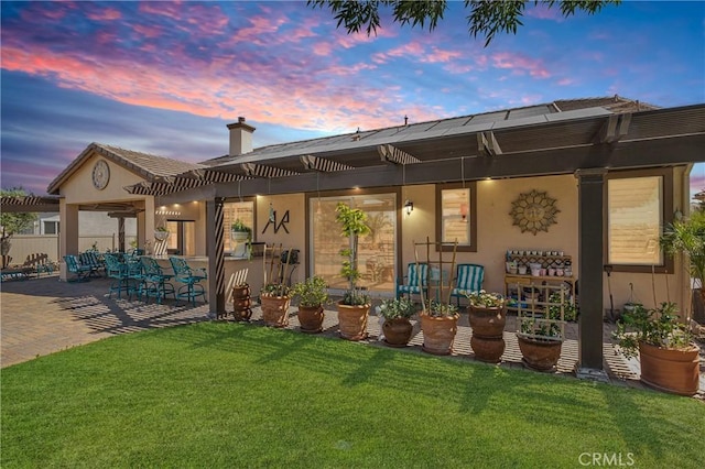 10844 Aster Ln, Apple Valley, CA 92308 - back of house at dusk featuring stucco siding, a patio area, a lawn, a pergola, and a chimney