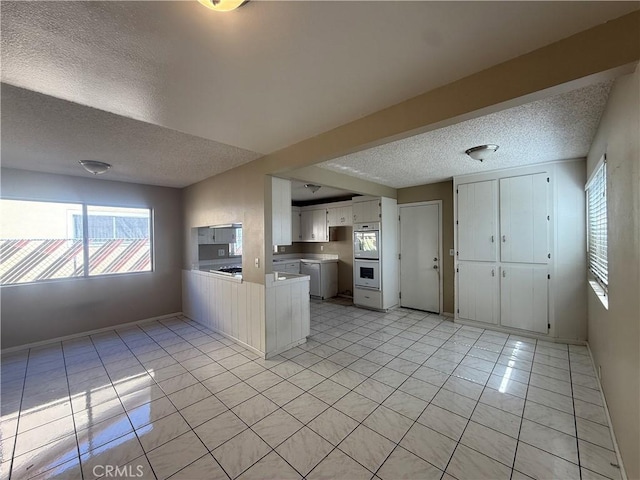 2854 Coronado Ave, San Diego, CA 92154 - kitchen featuring a textured ceiling, light tile patterned floors, a peninsula, white double oven, and white cabinets