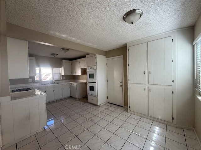 2854 Coronado Ave, San Diego, CA 92154 - kitchen featuring double oven, tile counters, stainless steel gas cooktop, white cabinets, and a textured ceiling