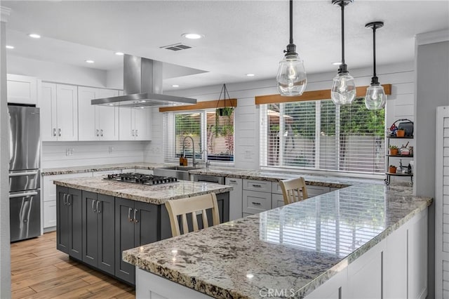 3652 San Joaquin Ave, Los Alamitos, CA 90720 - kitchen featuring white cabinetry, island exhaust hood, appliances with stainless steel finishes, a peninsula, and light wood-type flooring