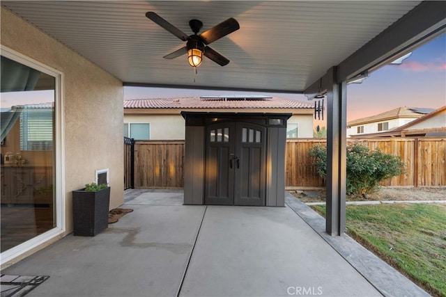 3558 Mt San Gorgonia Ave, Rosamond, CA 93560 - patio terrace at dusk featuring a storage unit, a patio area, a fenced backyard, and ceiling fan