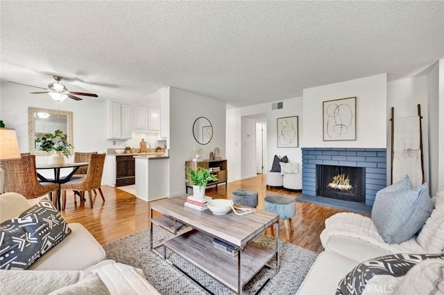 17574 Vandenberg Ln Unit 1, Tustin, CA 92780 - living area with a textured ceiling, light wood-type flooring, a brick fireplace, and ceiling fan