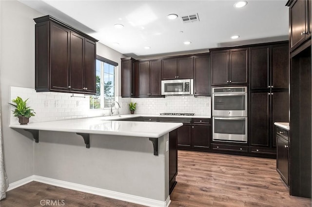 28419 Sunflower St, Highland, CA 92346 - kitchen featuring appliances with stainless steel finishes, a breakfast bar, dark brown cabinets, a peninsula, and light countertops