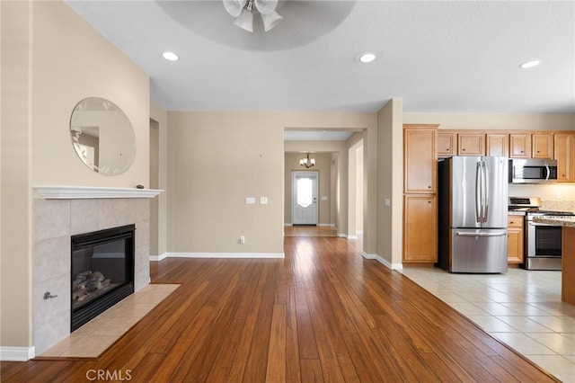 26135 Palm Breeze Ln, Menifee, CA 92586 - kitchen with appliances with stainless steel finishes, a ceiling fan, a tiled fireplace, light wood-style flooring, and recessed lighting