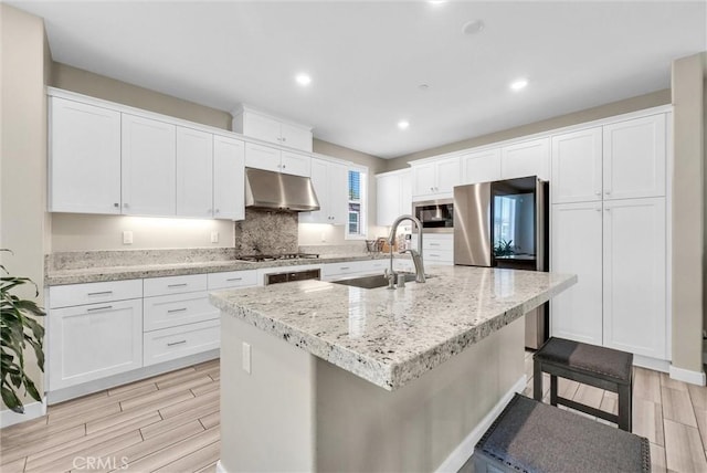 40 Riverton St, Phillips Ranch, CA 91766 - kitchen with under cabinet range hood, wood tiled floors, white cabinetry, a kitchen breakfast bar, and an island with sink