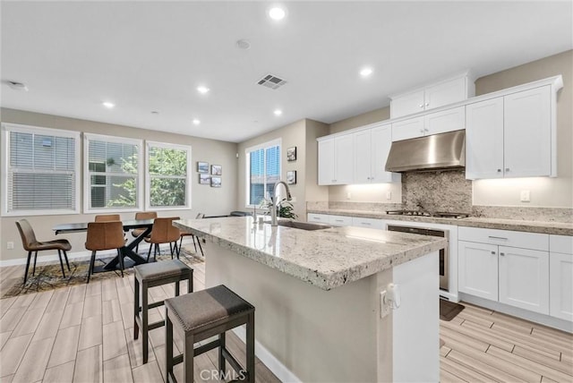 40 Riverton St, Phillips Ranch, CA 91766 - kitchen featuring under cabinet range hood, wall oven, wood tiled floors, a kitchen island with sink, and tasteful backsplash