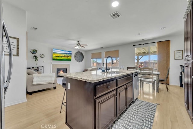 3026 Neary Ct, Rosamond, CA 93560 - kitchen featuring stainless steel dishwasher, a glass covered fireplace, ceiling fan, dark brown cabinets, and light wood-style flooring