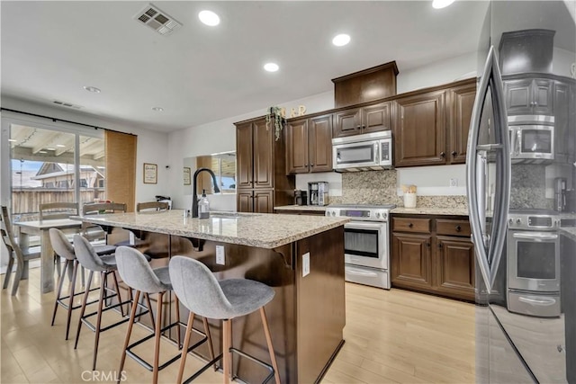 3026 Neary Ct, Rosamond, CA 93560 - kitchen with stainless steel appliances, an island with sink, a breakfast bar area, light stone counters, and light wood-style floors