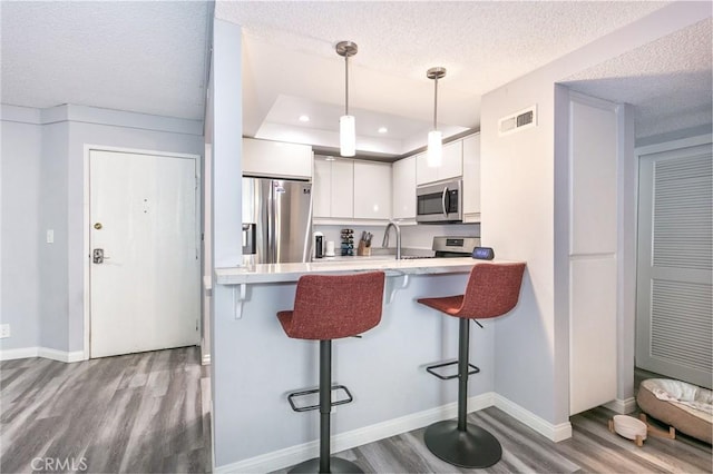 7800 Topanga Canyon Blvd Unit 324, Canoga Park, CA 91304 - kitchen with appliances with stainless steel finishes, wood finished floors, white cabinetry, a kitchen bar, and a peninsula