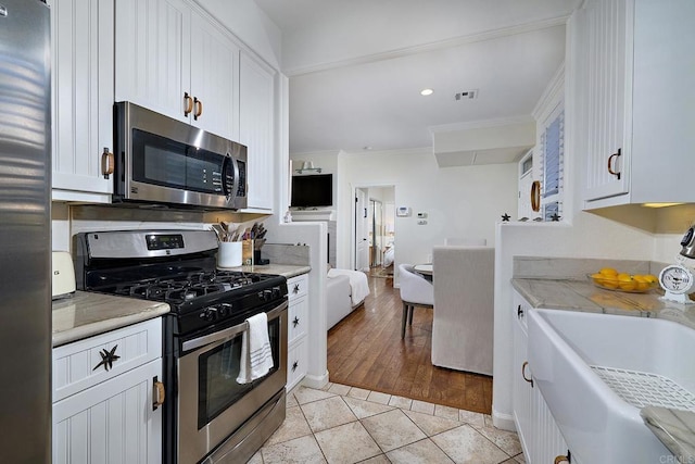 3521 Caminito El Rincon Unit 307, San Diego, CA 92130 - kitchen with stainless steel appliances, crown molding, white cabinetry, light countertops, and light tile patterned flooring