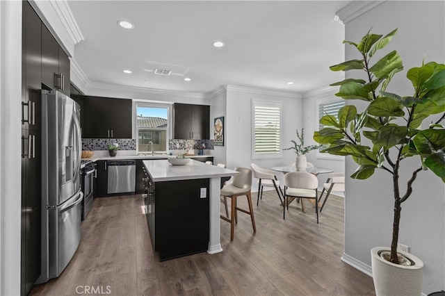 17557 Newland St Unit 101, Huntington Beach, CA 92647 - kitchen with stainless steel appliances, light countertops, dark cabinetry, a kitchen bar, and decorative backsplash