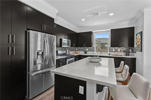 17557 Newland St Unit 101, Huntington Beach, CA 92647 - kitchen featuring stainless steel appliances, dark cabinetry, a breakfast bar, ornamental molding, and a kitchen island