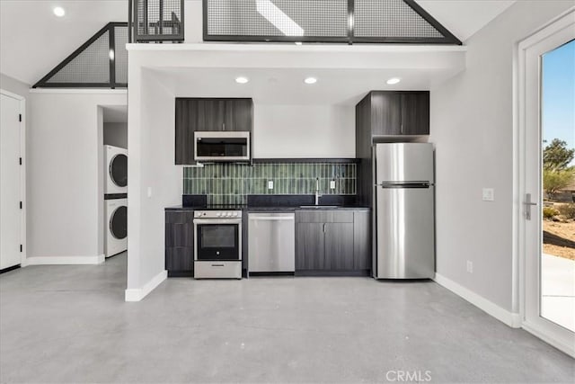 61850 Alta Mura Dr, Joshua Tree, CA 92252 - kitchen with stainless steel appliances, stacked washing machine and dryer, finished concrete floors, dark countertops, and decorative backsplash