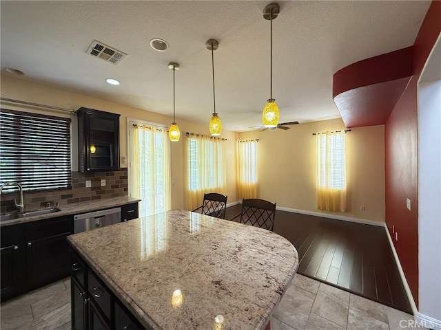 24112 Joshua Dr, Valencia, CA 91354 - kitchen featuring dishwasher, dark cabinets, a center island, tasteful backsplash, and light stone counters
