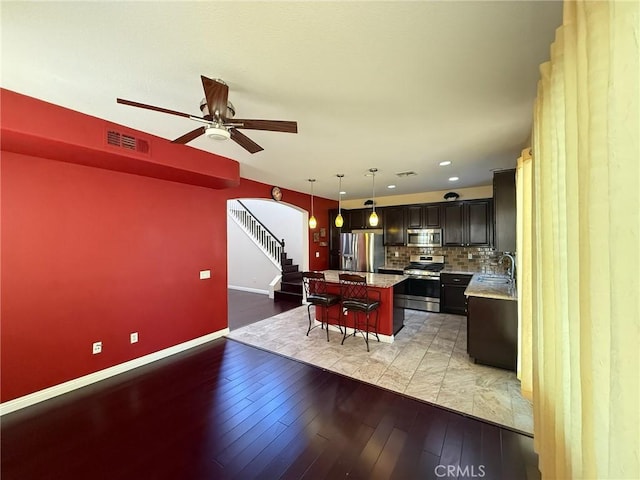 24112 Joshua Dr, Valencia, CA 91354 - kitchen with appliances with stainless steel finishes, a kitchen bar, arched walkways, a ceiling fan, and light wood-type flooring