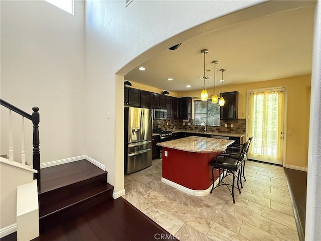 24112 Joshua Dr, Valencia, CA 91354 - kitchen featuring appliances with stainless steel finishes, a center island, a breakfast bar, arched walkways, and decorative backsplash