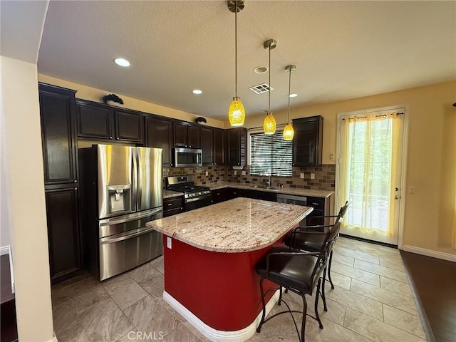 24112 Joshua Dr, Valencia, CA 91354 - kitchen featuring appliances with stainless steel finishes, tasteful backsplash, light stone counters, a kitchen island, and a breakfast bar area