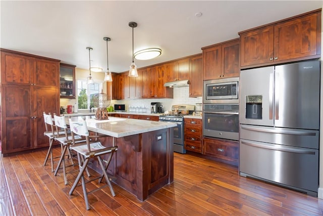 9401 Whispering Pines Rd, Frazier Park, CA 93225 - kitchen with appliances with stainless steel finishes, under cabinet range hood, dark wood-style flooring, and decorative backsplash