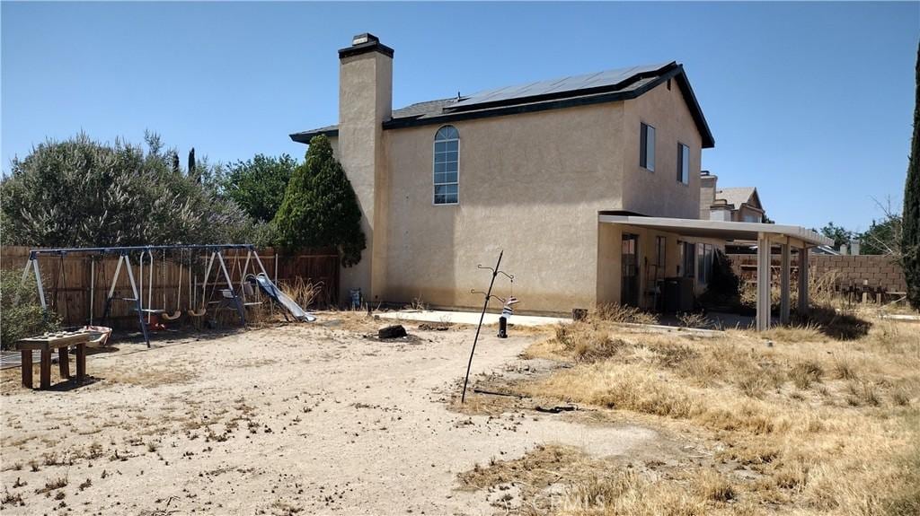 3096 Sedona St, Rosamond, CA 93560 - back of house featuring roof mounted solar panels, a chimney, a playground, and stucco siding