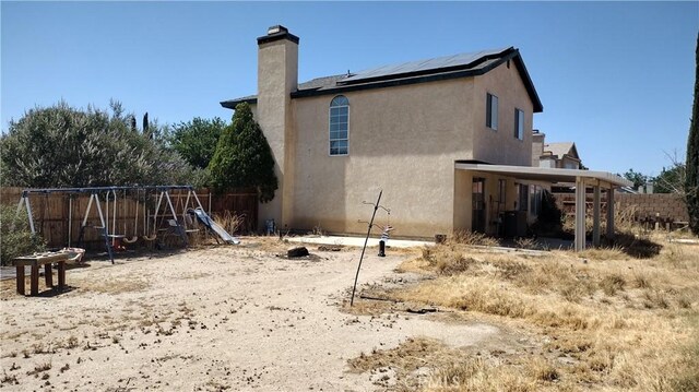 3096 Sedona St, Rosamond, CA 93560 - back of house featuring roof mounted solar panels, a chimney, a playground, and stucco siding