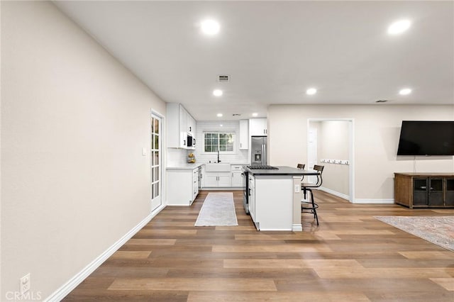 716 N Tulare Way, Upland, CA 91786 - kitchen with stainless steel refrigerator with ice dispenser, a breakfast bar, recessed lighting, white cabinetry, and wood finished floors