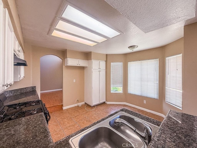 16702 Canoe Cv, Moreno Valley, CA 92551 - kitchen featuring arched walkways, white cabinetry, light tile patterned flooring, black gas range oven, and under cabinet range hood