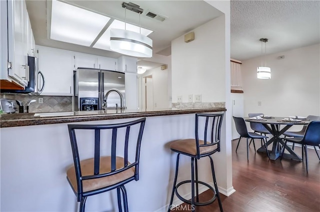7302 Bright Ave Unit B, Whittier, CA 90602 - kitchen with dark countertops, appliances with stainless steel finishes, dark wood finished floors, decorative backsplash, and a kitchen breakfast bar