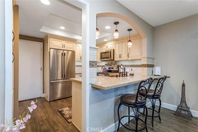 23130 Yvette Ln, Valencia, CA 91355 - kitchen with appliances with stainless steel finishes, a tray ceiling, a peninsula, dark wood finished floors, and decorative backsplash