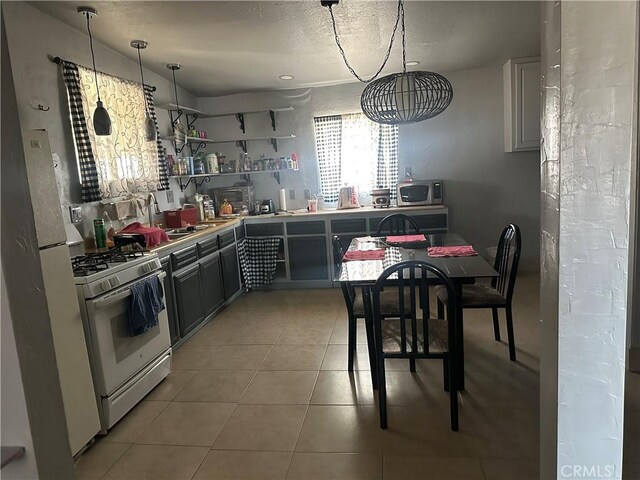 3938 Kreuer Rd, Phelan, CA 92371 - kitchen with white gas range, light tile patterned flooring, open shelves, stainless steel microwave, and a textured ceiling