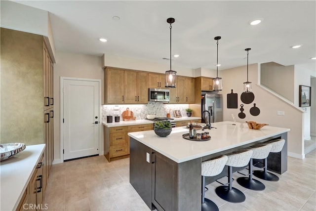 17163 Kent St, Hesperia, CA 92345 - kitchen with appliances with stainless steel finishes, a kitchen island with sink, backsplash, light countertops, and decorative light fixtures