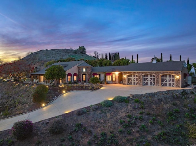 30419 Canyon Estates Rd, Vista, CA 92084 - back of property at dusk featuring concrete driveway, stone siding, a garage, a mountain view, and a chimney