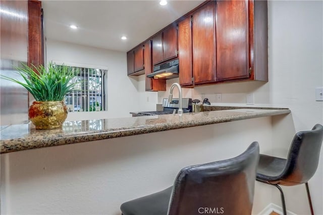 4140 Workman Mill Rd Unit 78, Whittier, CA 90601 - kitchen with under cabinet range hood, recessed lighting, light stone countertops, a kitchen breakfast bar, and stove