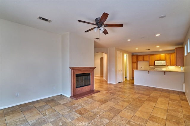 1660 Snowberry Rd, Beaumont, CA 92223 - unfurnished living room featuring arched walkways, stone tile flooring, recessed lighting, a ceiling fan, and a glass covered fireplace