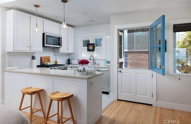 31907 9th Ave, Laguna Beach, CA 92651 - kitchen with a peninsula, stainless steel appliances, white cabinetry, light wood-style floors, and light countertops